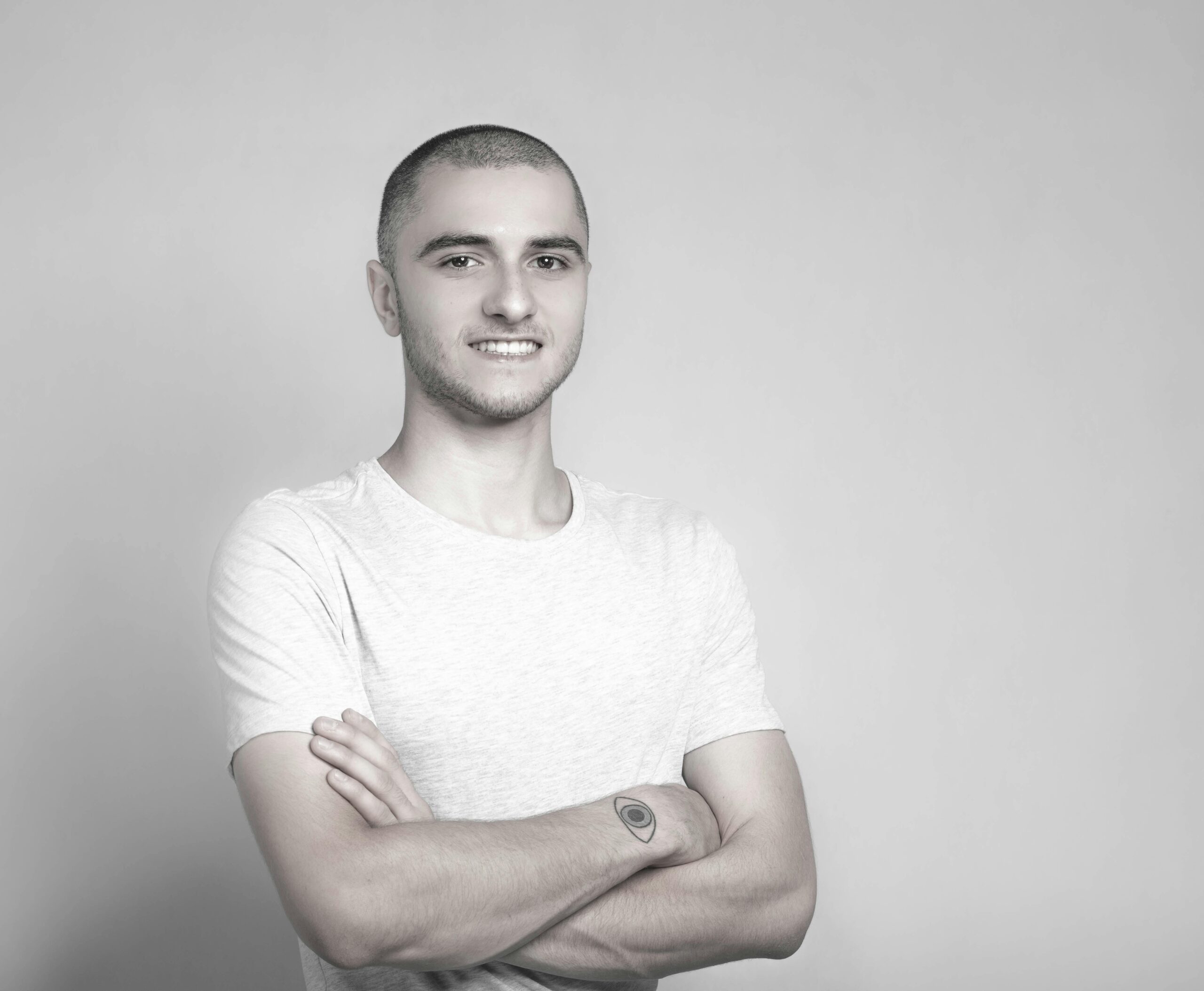 Grayscale portrait of a confident young man with crossed arms and a subtle smile.